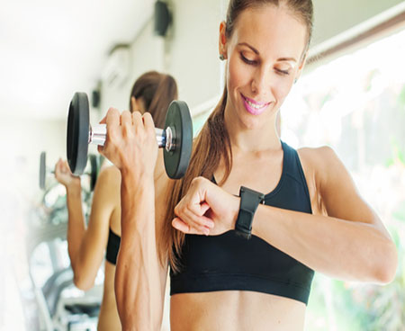 A woman checks her fitness tracker while weightlifting