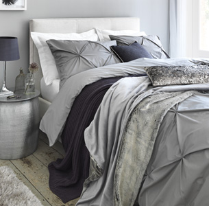 Knitted and faux fur throws layered on grey textured duvet.