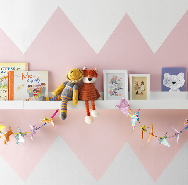 Books, toys and photo frames on white shelf with pink triangle paint effect.