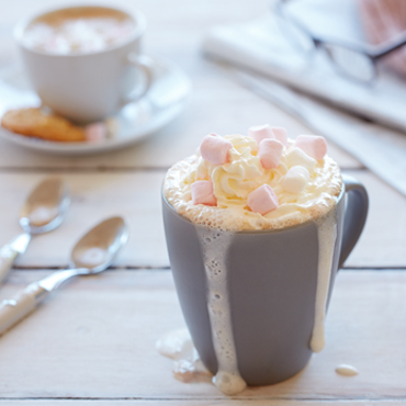 A cup of hot chocolate, complete with whipped cream and marshmallows, sit in a grey mug.