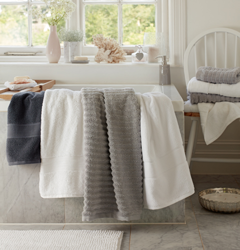 Fluffy towels in grey and white lay over the side of the bath.