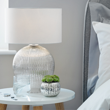 A chrome bedside table lamp with white circular shade sits on a white bedside table.