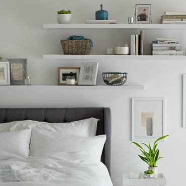 White floating shelves sit above a grey bed with ornaments, books and vases.