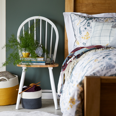 An image of a cream and wooden dining room chair being used as a bedside table.