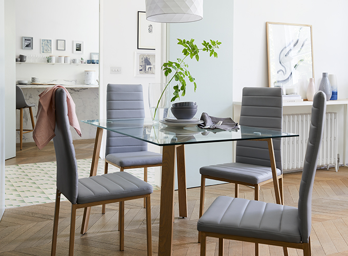 A glass-topped dining table with 4 light grey chairs.