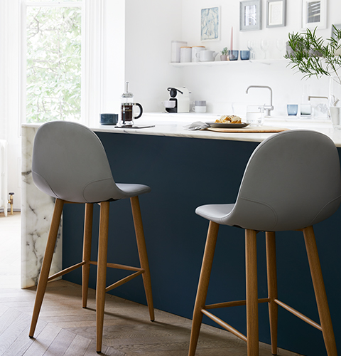 A dark blue and marble kitchen counter with grey and wood Scandi-style stools.