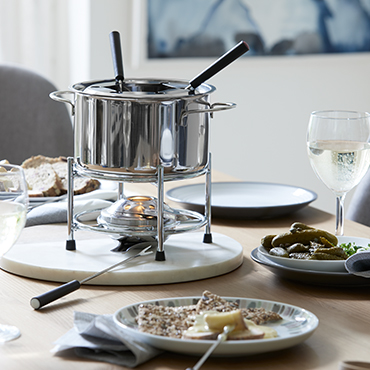 A silver fondue set in the centre of a wooden table.