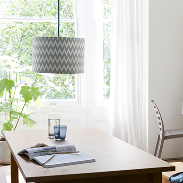 A wooden dining table with a grey patterned pendant light.