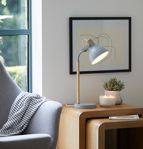 A grey armchair and stacking side tables with candle, lamp and succulent.