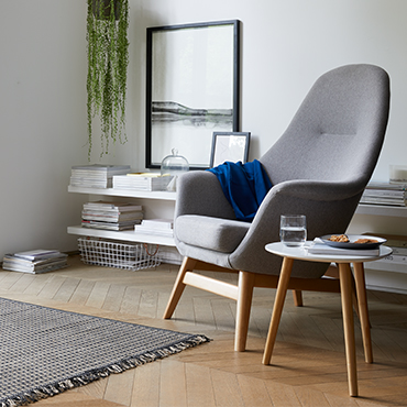 A grey armchair with curved table and grey rug.