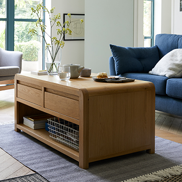 A curved wooden coffee table in the centre of a blue Scandi lounge.