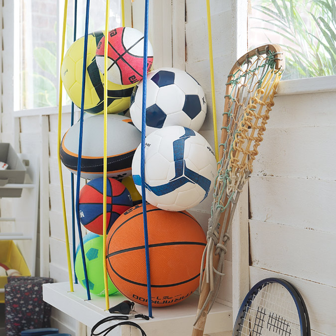 Image of footballs, rugby balls and other sports balls fixed to the wall by bungee wires.