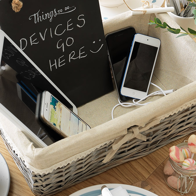 Image of a basket with sign reading 'Devices go here' and mobile phones and tablets in the basket.