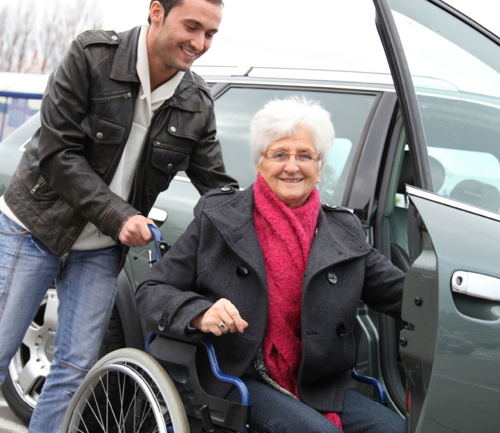 Woman in wheelchair being helped into car by man