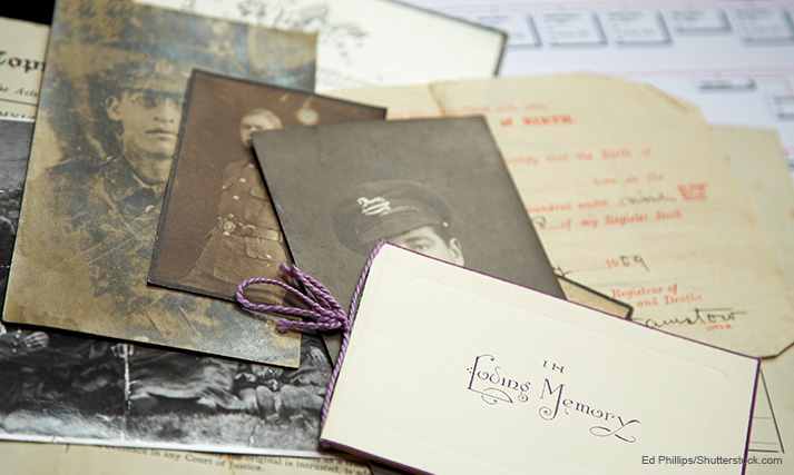 Collection of black and white photographs of a soldier, documents and an in loving memory card set spread on top of a family tree plan.