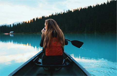 Image of a girl in an open kayak on a lake surrounded by fir trees.