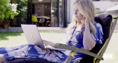 Image of a woman reclining on a sun lounger working on a laptop.