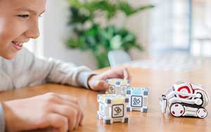 Lifestyle image of the Anki Cozmo robot on a table moving towads a boy.