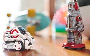 Lifestyle image of the Anki Cozmo roboton a table facing a grey toy robot.