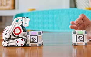 Lifestyle image of the Anki Cozmo robot pushing a block on a table.