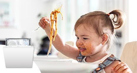 Toddler making a mess eating spagetti with a cut out image of a white Indesit dishwasher.