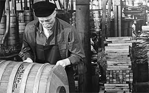 Black and white photograpg of a man working on a Miele branded wooden barrel in a factory.