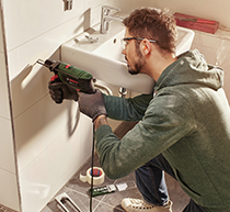 Image of someone using a corded impact drill to remove tiles.
