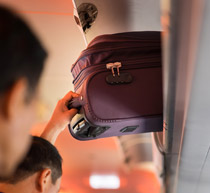 Image of someone on a plane putting their cabin luggage in overhead storage.