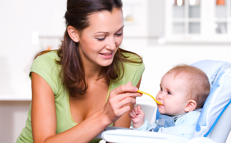Mum feeding baby with spoon in highchair.
