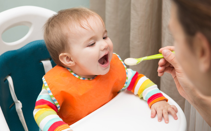 Mum spoon feeding a baby sitting in highchair.