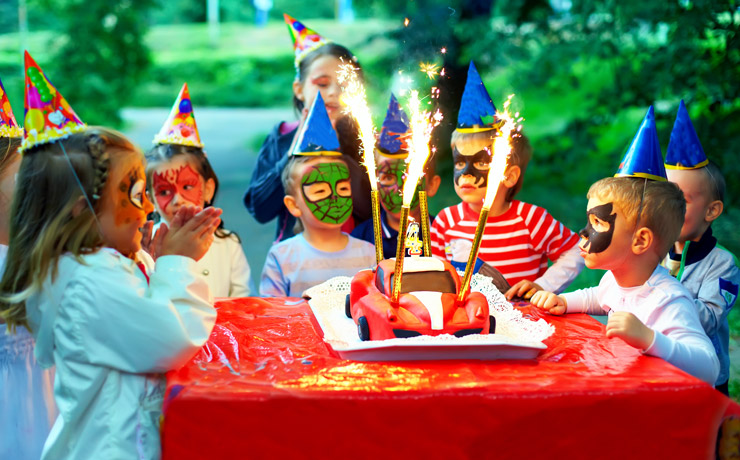 Children wearing party hats and face paint around a birthday cake.