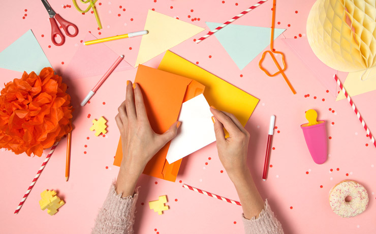 A woman's hands putting a paper invitation in colourful envelope.