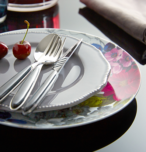 A stack of floral and embossed crockery and silver cutlery.