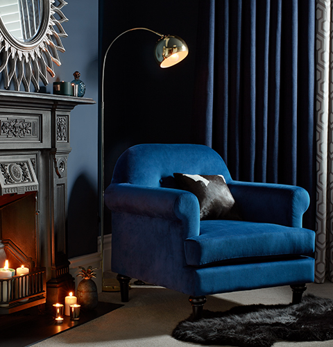 A cobalt blue accent chair sits in front of a black painted fireplace with chrome reading light and faux-fur black rug.