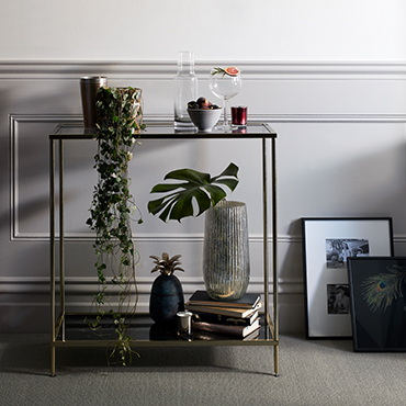 A black and gold side table is dressed with fairy lights, vases and stacks of books.