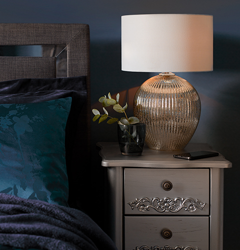 A chrome finish lamp sits on an ornate silver bedside table.