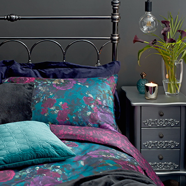 A floral duvet cover layered with teal velvet cushion.