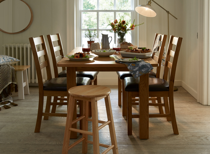 A wooden dining table in a lounge with light in the background.