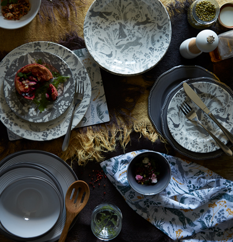 An overhead view of a dining table, with grey and cream coloured tableware in coordinationg woodland print designs.