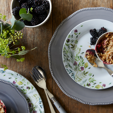 A blackberry crumble served in a ramakin, with a floral patterned plate underneath.