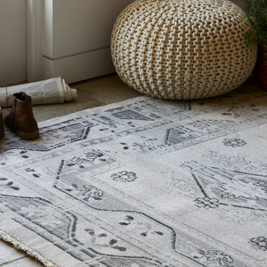 A distressed cream coloured antique Persian-style rug by a patio door. A pair of shoes and knitted cream pouffe lay by the rug.