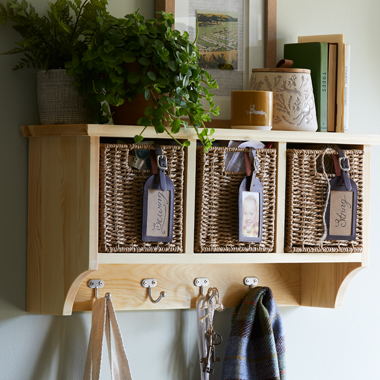 A wooden and wicker storage unit mounted on a sage coloured wall. We've attached leather luggage tags attached to the storage boxes for a homespun and handy edge.