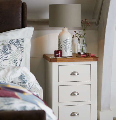 A two tone cream and oak-finish bedside table with leaf print bedside lamp.