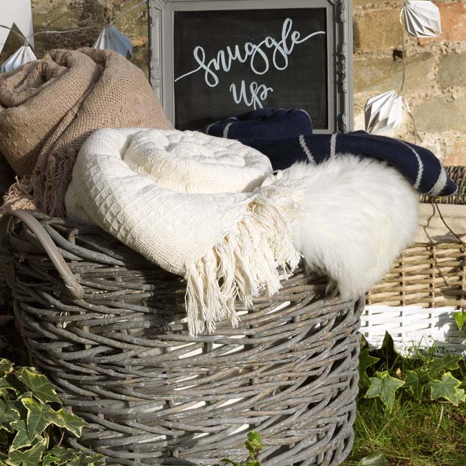A wicker basket with throws and blankets inside.