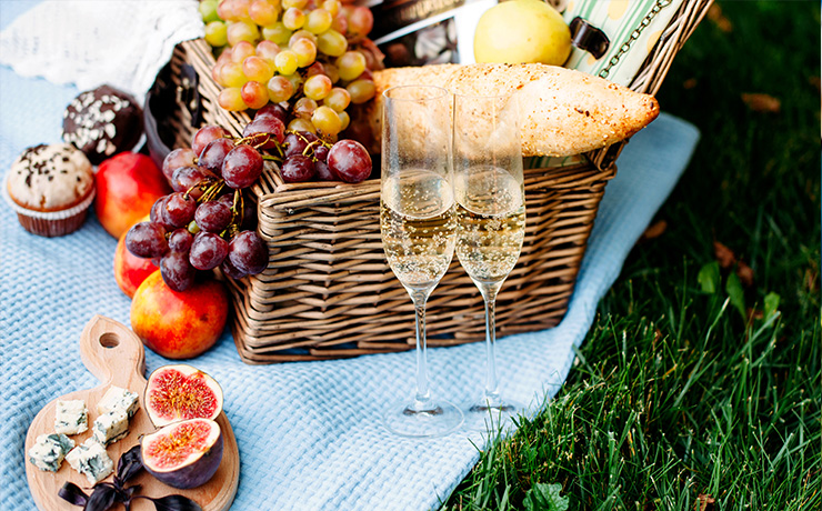 Image of a picnic with wine glasses, and a basket full of bread and grapes