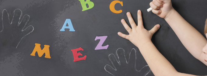 Child drawing round their hand on a blackboard with letter magnets on it.