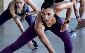 Image of a person in an exercise class reaching down to their feet across their body wearing a Fitbit Ionic.