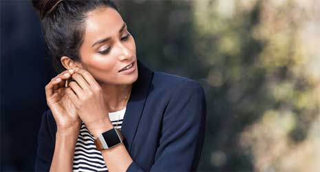 Image of a woman putting an earring in her ear wearing a Fitbit Ionic.