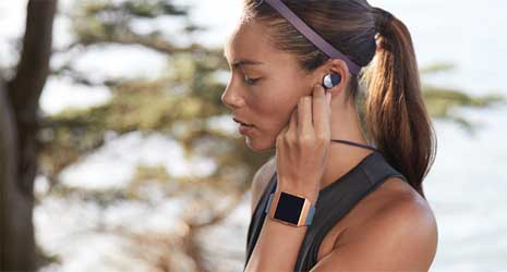 Image of a woman outside wearing Fitbit Flyer earphones and a Fitbit Ionic smartwatch.