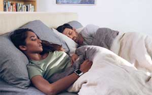 Image of a couple sleeping in bed, the woman wearing a Fitbit Ionic.